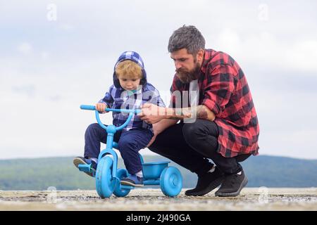 Il ragazzino impara a guidare una bicicletta con il suo papà. Papà insegnando a figlio di andare in bicicletta. Padre che insegna il ciclismo a suo figlio. Giorno dei padri. Foto Stock