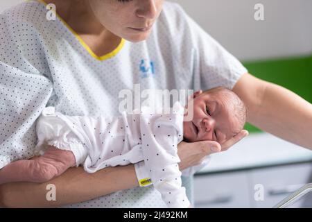 la mamma che ha appena partorito in ospedale tiene il suo neonato in braccia faccia in giù per sbarazzarsi di gas e prevenire coliche nel bambino. neonato h Foto Stock