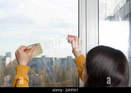 Una donna tape le finestre nel suo appartamento, nastro a nastro, durante la guerra. Evitare il pericolo di schegge se il finestrino viene urtato dal getto Foto Stock