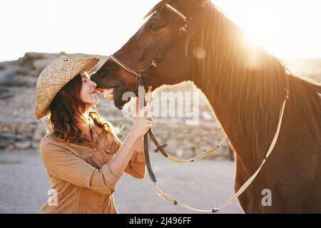 Giovane donna contadina che ha momento tenero baciando il suo cavallo al ranch fattoria - Focus on Face Foto Stock