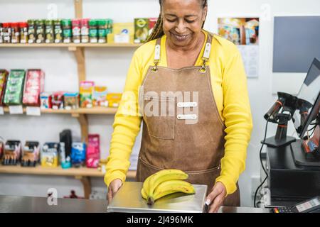 Donna africana anziana che lavora all'interno del mercato biologico fresco - Focus principale sulla bocca femminile Foto Stock