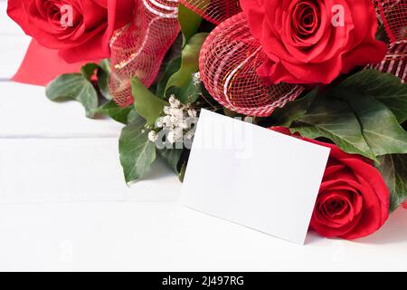 Bouquet fresco di rose rosse fresche con cartoncino bianco vuoto su sfondo bianco di legno. Concetto di biglietto festivo, luogo per il testo Foto Stock