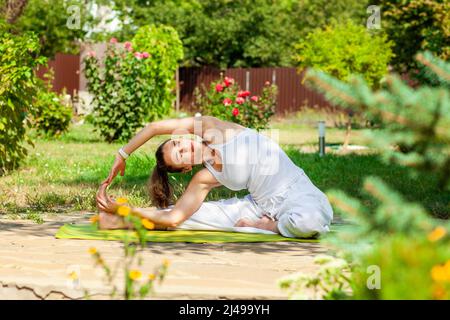 La giovane donna pratica yoga nel giardino estivo - capovolta la testa al ginocchio, parivritta Janu Shirshasana. Foto Stock