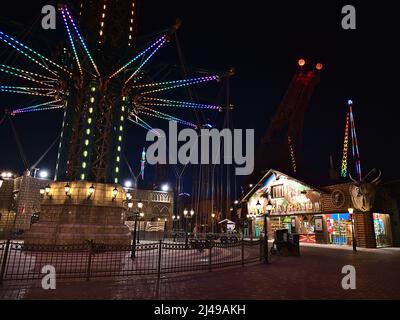 Vista notturna del famoso parco divertimenti Wurstelprater a Vienna, Austria, con torre di lancio illuminata e negozi in serata. Foto Stock