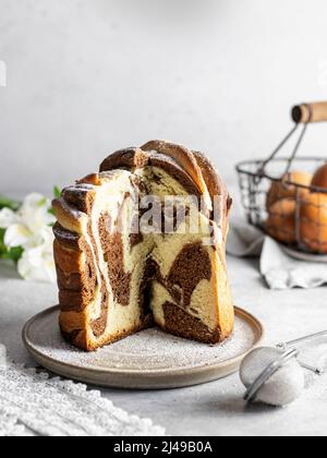 Torta di Pasqua tagliata kraffin cosparso di zucchero a velo. Primo piano di torta in casa a due colori. Crociera. Orientamento verticale Foto Stock