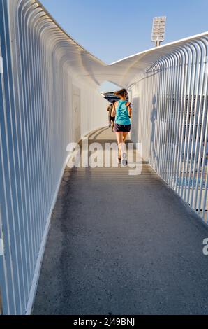 Un uomo e una donna che corrono su un ponte pedonale stretto (Erskine link) nel sole del tardo pomeriggio a Perth, Australia Occidentale Foto Stock