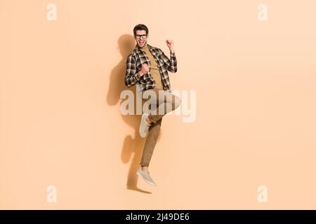 Vista a tutta lunghezza del corpo di attraente allegro ragazzo che salta danzando divertirsi isolato su sfondo beige color pastello Foto Stock