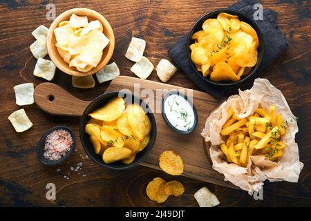 Cibo o spuntini malsani. Tutti i classici spuntini di patate con arachidi, anelli di popcorn e cipolle e pretzel salati in piatti da ciotola su vecchio sfondo di legno. Foto Stock