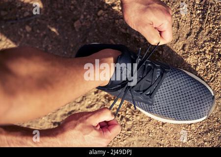 Pronto a correre il suo cuore all'aperto. Colpo ad angolo alto di un uomo irriconoscibile che lega le sue scarpe mentre si esercita all'aperto. Foto Stock