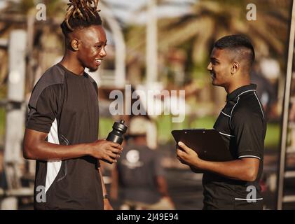 Bastone con me e youll andare lontano. Scatto di un giovane uomo che pianifica la sua routine di allenamento con il suo personal trainer. Foto Stock