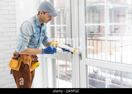 Addetto alle costruzioni che mette in casa il nastro di schiuma sigillante sulla finestra Foto Stock