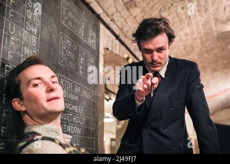 Londra, Regno Unito, 13th aprile 2022. Christopher Styles e Timothy Styles in una scena di interrogazione. Immersive Theatre società parabolica presenta il remount del loro successo 'illecito segnali Bletchley'. Il pubblico può interagire, passeggiare e lavorare insieme a personaggi famosi del codice governativo e della Cipher School di Bletchley Park per rompere L'ENIGMA, mentre i segreti scomodi più vicini a casa minacciano di essere svelati. Lo spettacolo si svolge presso la NUOVA E coinvolgente CRIPTA del teatro parabolico con Christopher Styles, Amelia Stephenson, Timothy Styles e Beth Jay. Foto Stock