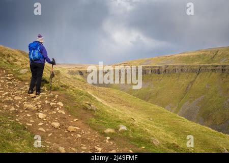 08.04.2022 Dufton, Westmorland, Regno Unito. Camminatore di collina femminile in blu e viola dirigendosi verso High Cup Nick nel nord Pennines Foto Stock