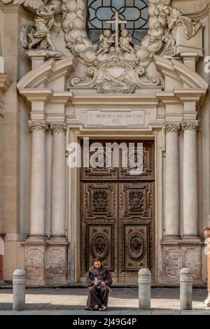 Un sacerdote legge seduto davanti alla Chiesa Parrocchiale della Santissima Annunziata a Parma Foto Stock