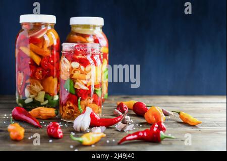 Varietà di peperoni, spezie e aglio in vasetti fermentanti, una ricca fonte di probiotici, per fare salsa calda fatta in casa su uno sfondo rustico. Foto Stock