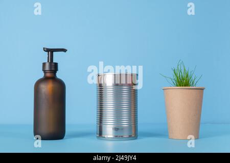 Riciclare tazze di carta, lattine, vetro. Prodotti usati su sfondo blu. Germogli germogliati da una tazza di cartone Foto Stock