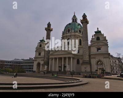 Vista della famosa chiesa di Karlskirche situato in piazza Karlsplatz nel centro storico di Vienna, Austria in una giornata nuvolosa in primavera con gente rilassante. Foto Stock