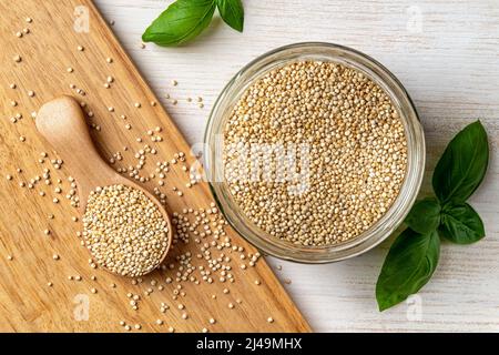 Semi bianchi di quinoa in un vaso di vetro e cucchiaio di legno su tavola bianca di legno. Grani di quinoa secchi per la dieta senza glutine. Chenopodium quinoa superfood. Foto Stock