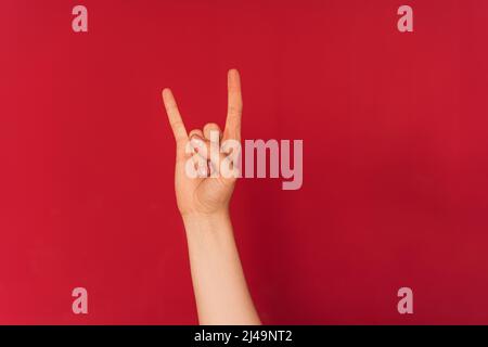 La mano della donna mostra il simbolo del rock and roll su sfondo rosso Foto Stock