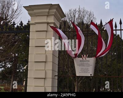 Vista della bacheca con bandiere all'ingresso del parco pubblico Burggarten nel centro storico di Vienna, Austria con recinzione in ferro nelle giornate nuvolose. Foto Stock