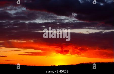 Astratto cielo bruciante al tramonto. Le nuvole rosse all'orizzonte sono illuminate dalla luce del sole serale. Foto Stock
