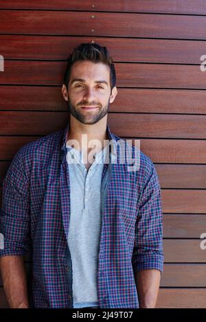 HES un ragazzo facile andare. Ritratto di un bell'uomo in piedi contro un muro di legno. Foto Stock