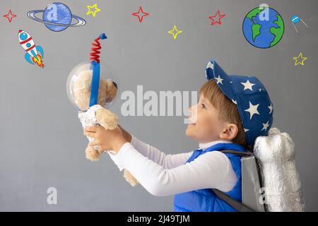 Bambino felice che gioca con il razzo giocattolo. Il bambino tiene orsacchiotto contro il fondo della parete di calcestruzzo. Ragazzo finge di essere astronauta. Imagination e bambini dr Foto Stock