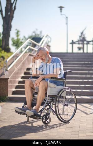 Un uomo disabile in una sedia a rotelle all'aperto guardando premuroso Foto Stock