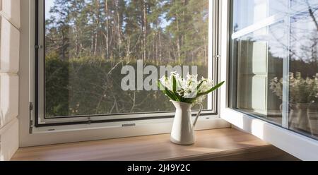 Finestra bianca con rete di mosuito in una casa rustica in legno che si affaccia sul giardino fiorito. Foto Stock