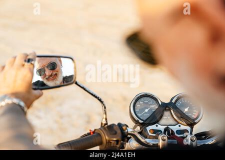 Uomo anziano audace che guarda lo specchietto retrovisore mentre guida la moto la giornata estiva Foto Stock