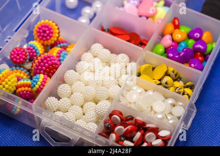 Scatola in plastica con piccoli accessori per agugliare in celle separate su sfondo blu. Foto Stock