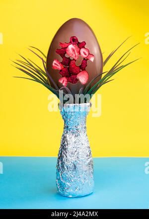 Uovo di Pasqua al cioccolato e decorazione su sfondo blu e giallo vibrante Foto Stock