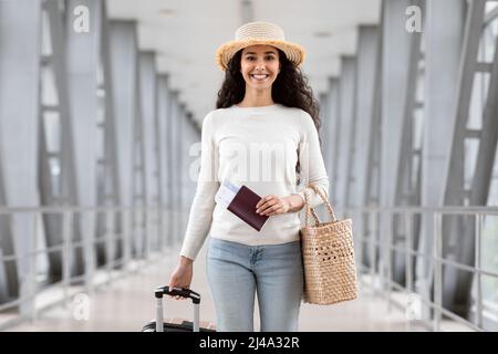 Ritratto di felice donna mediorientale che indossa il cappello di paglia in posa in aeroporto Foto Stock