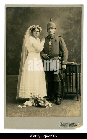 Meraviglioso, chiaro e originale ritratto di uno studio di carte armadio dell'epoca della prima Guerra Mondiale del soldato tedesco bavarese dell'Impero tedesco o dello Stato Imperiale della Germania con la sua bide, indossa un "Pickelhaube" (casco a punta) con copertura Uberzug e indossa speroni sugli stivali - cavalleria / cavaliere. Indossa con orgoglio una croce al merito militare bavarese della prima guerra mondiale sulla sua uniforme. È vestita con un abito bianco da sposa con velo. Sono una coppia attraente. Dallo studio fotografico di Joseph Werner, a Isartorplatz Munchen (Monaco di Baviera) , Baviera, Germania. Soldati della prima guerra mondiale soldati della prima guerra mondiale. Intorno al 1914 Foto Stock