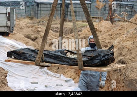 BUCA, UCRAINA - 13 APRILE 2022 - un esperto in un vestito protettivo guarda un sacchetto di resti umani con una persona in ritardo che viene tolta da un'altra tomba di massa dove i civili uccisi dagli invasori russi sono sepolti durante l'esumazione, Buca, Regione di Kiev, Ucraina settentrionale. Credit: Ukrinform/Alamy Live News Foto Stock