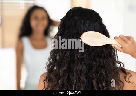 Curly Brunette Lady spazzolando i suoi capelli lunghi e belli con il pettine di bambù Foto Stock