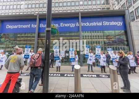 Londra, Regno Unito. 13 aprile 2022. Gli attivisti ambientalisti della ribellione per l'estinzione organizzano una protesta pacifica al di fuori del Department for Business, Energy & Industrial Strategy a Londra. I manifestanti in camici bianchi da laboratorio hanno cartelli che recano "NIENTE PETROLIO", "NIENTE GAS" e "TRANSIZIONE GIUSTA", che chiedono un'azione urgente sulla dipendenza dai combustibili fossili e una transizione energetica equa. Uno striscione nero sul terreno recita “COMBUSTIBILI FOSSILI ORA” con il simbolo della ribellione dell’estinzione. La protesta evidenzia la preoccupazione dell'opinione pubblica per la politica climatica e la strategia energetica. Penelope Barritt/Alamy Live News Foto Stock