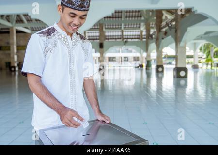 musulmano che paga un po 'di zakat carità utilizzando denaro presso la moschea Foto Stock