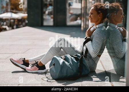 Donna in abbigliamento sportivo seduta all'aperto e ascolto di musica tramite cuffie Foto Stock