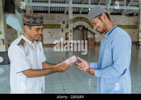 musulmano che paga un po 'di zakat carità utilizzando denaro presso la moschea Foto Stock