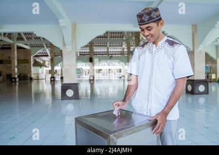 musulmano che paga un po 'di zakat carità utilizzando denaro presso la moschea Foto Stock