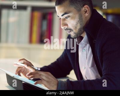 Mettere la tecnologia in prima linea nella sua carriera. Scatto di un giovane concentrato che lavora su un tablet digitale nel suo ufficio domestico in prima serata. Foto Stock