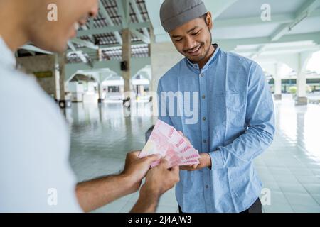 musulmano che paga un po 'di zakat carità utilizzando denaro presso la moschea Foto Stock