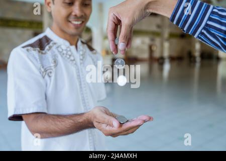 musulmano che paga un po 'di zakat carità utilizzando denaro presso la moschea Foto Stock