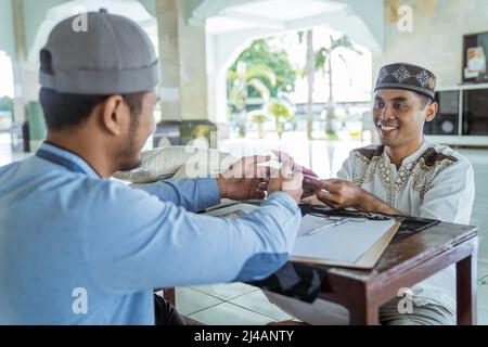 musulmano che paga un po 'di zakat carità utilizzando denaro presso la moschea Foto Stock