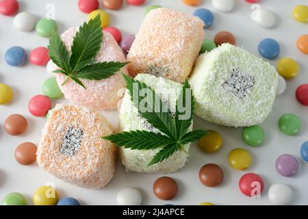 Dessert di cannabis. Delizia turca con fiocchi di cocco e confetti colorati da vicino. Foglie verdi di cmarijuana su sfondo bianco. Disposizione dell'orlo Foto Stock