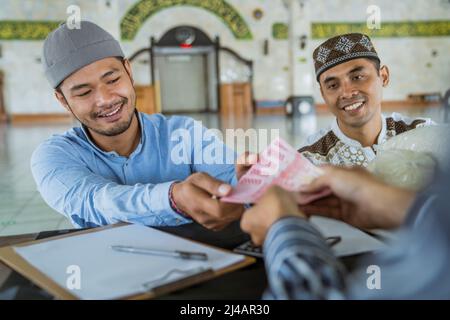 musulmano che paga un po 'di zakat carità utilizzando denaro presso la moschea Foto Stock