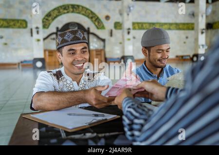 musulmano che paga un po 'di zakat carità utilizzando denaro presso la moschea Foto Stock