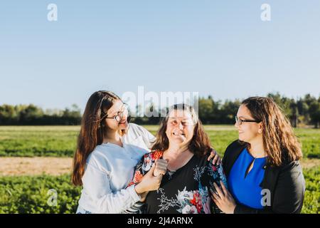 Famiglia femminile sorridente e abbracciata in campo in un pomeriggio di sole. Giornata delle madri. Foto Stock