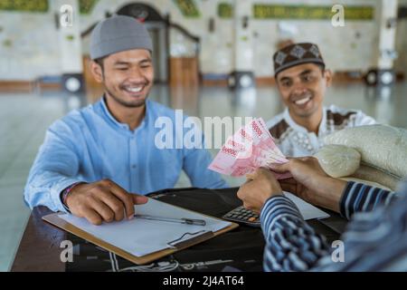 musulmano che paga un po 'di zakat carità utilizzando denaro presso la moschea Foto Stock